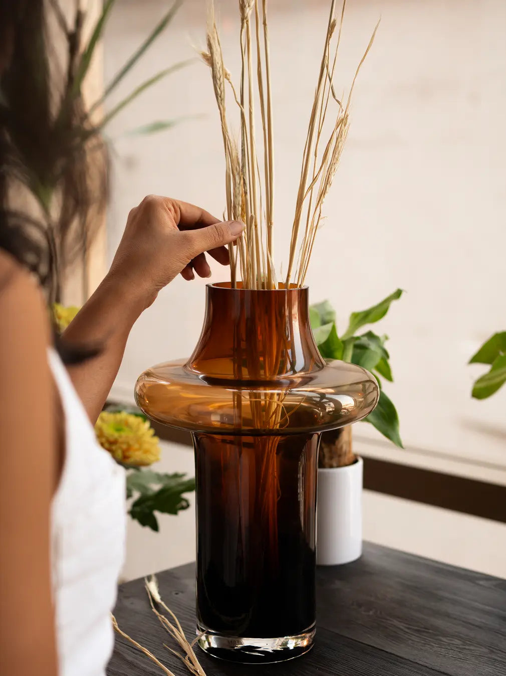 Hand arranging dried stems in Halo Amber Glass Vase - Large, amber glass flower vase with plants.