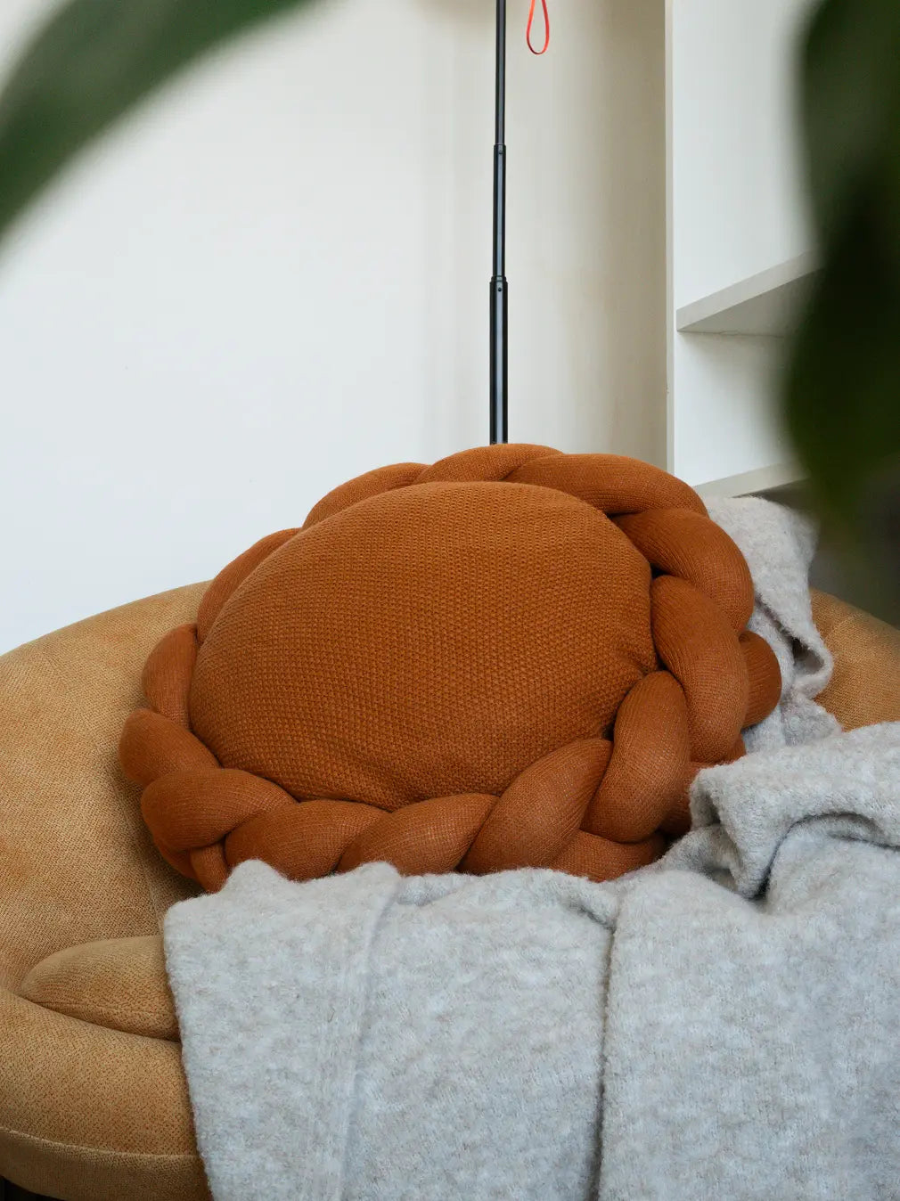 Round mustard wool cushion with sculptural braided edge styled on sofa chair