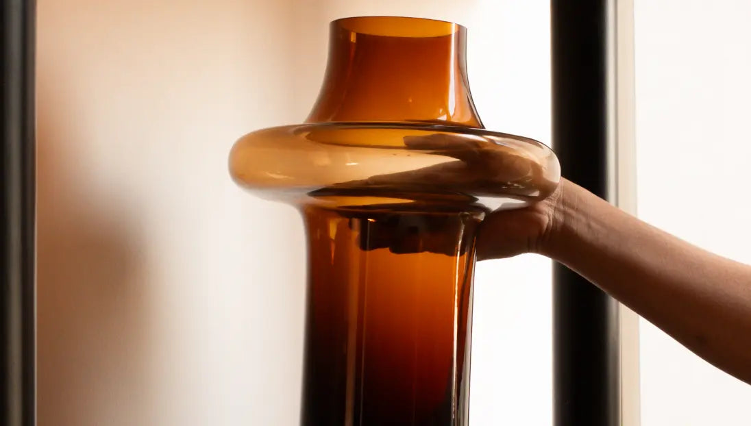 Hand lifting Halo Amber Glass Vase near window, tall amber glass vase for modern decor.