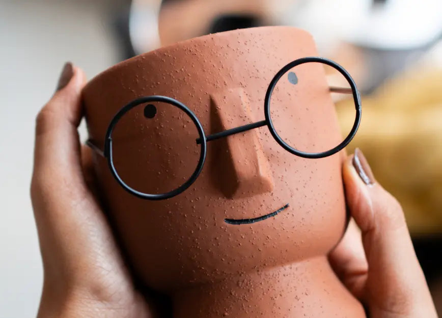 Handheld Jojo Brown indoor planter showing minimal face design and removable metal glasses