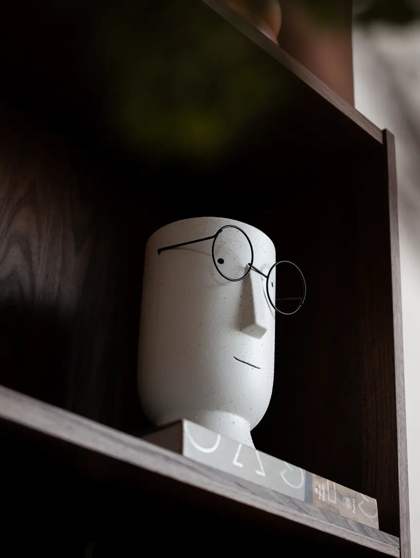 Jojo white ceramic planter with minimalist face and metal glasses on wooden shelf