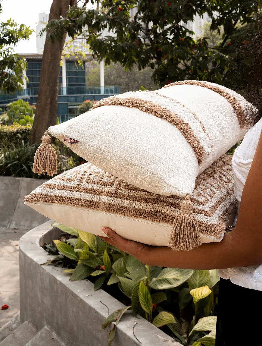 Person holding decorative pillows with tassels in an outdoor setting