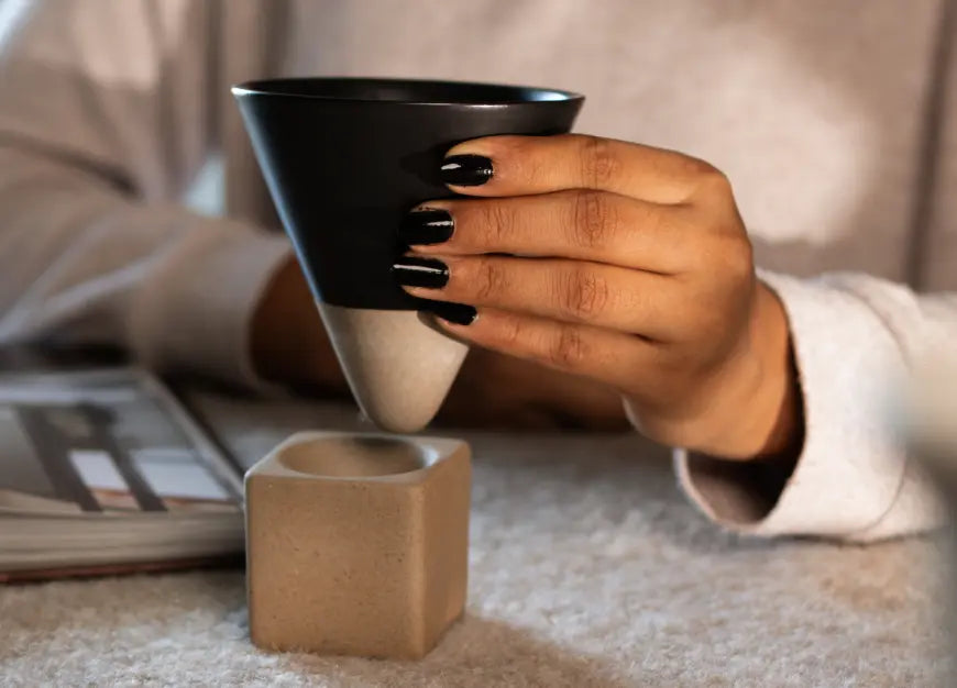 Black ceramic coffee cup held in hand with balanced cone design