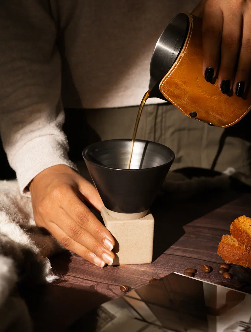 Pouring coffee into black ceramic cup with stable geometric base