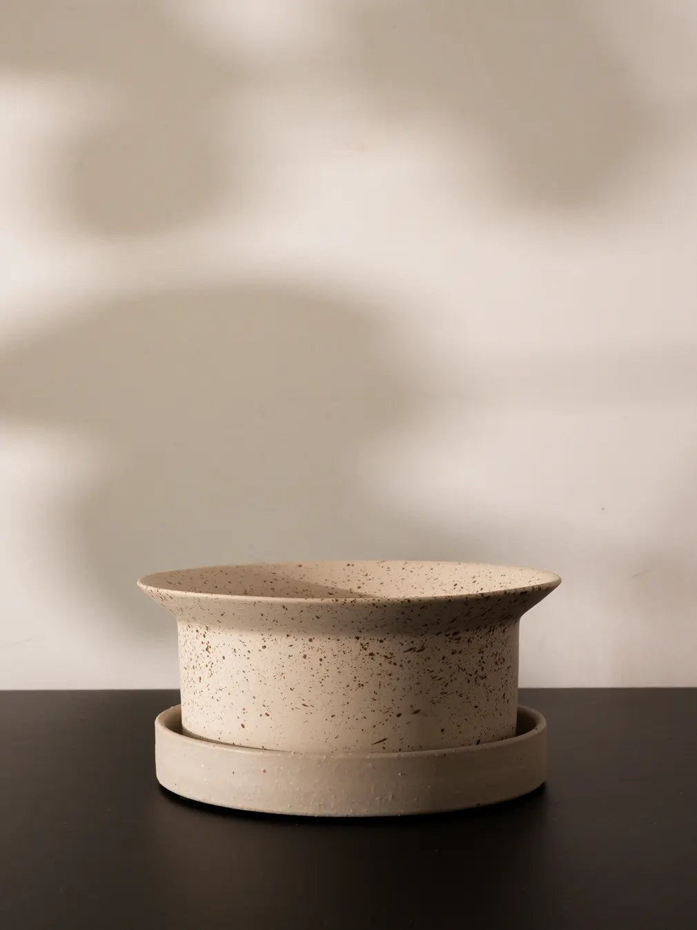 Close-up of empty Kora Ceramic Planter with speckled ink dot finish and matching saucer on black table