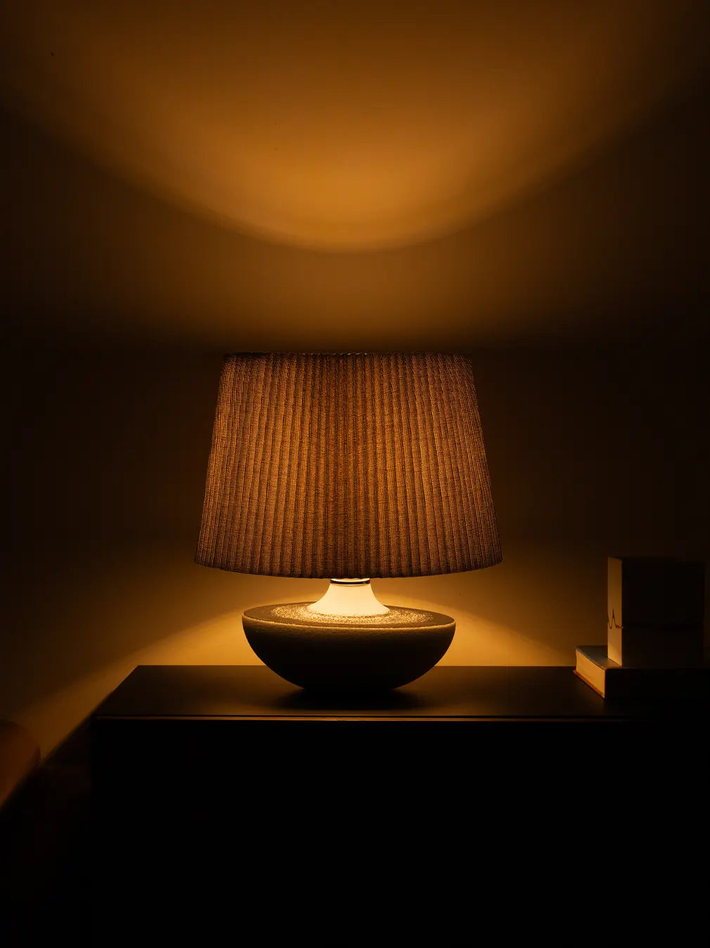 Table lamp with a textured shade casting a warm glow in a dimly lit room.