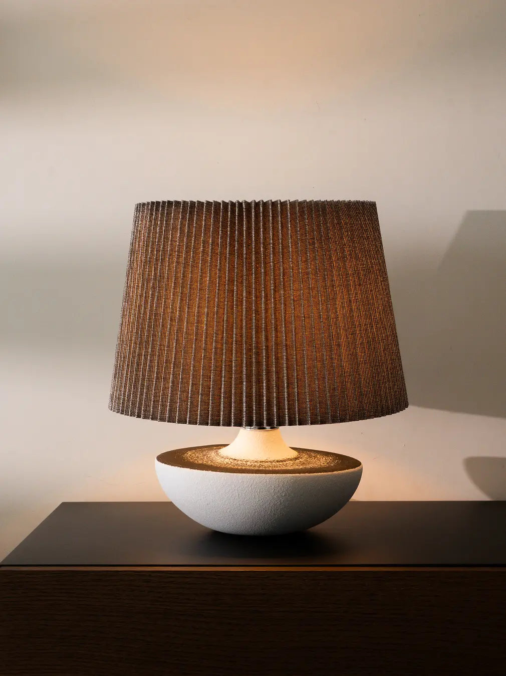 Table lamp with a pleated brown shade and textured white base on on wooden surface for modern interiors