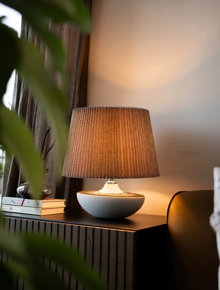 Premium Ceramic Table lamp with a textured brown shade on a wooden surface, surrounded by books and a plant.