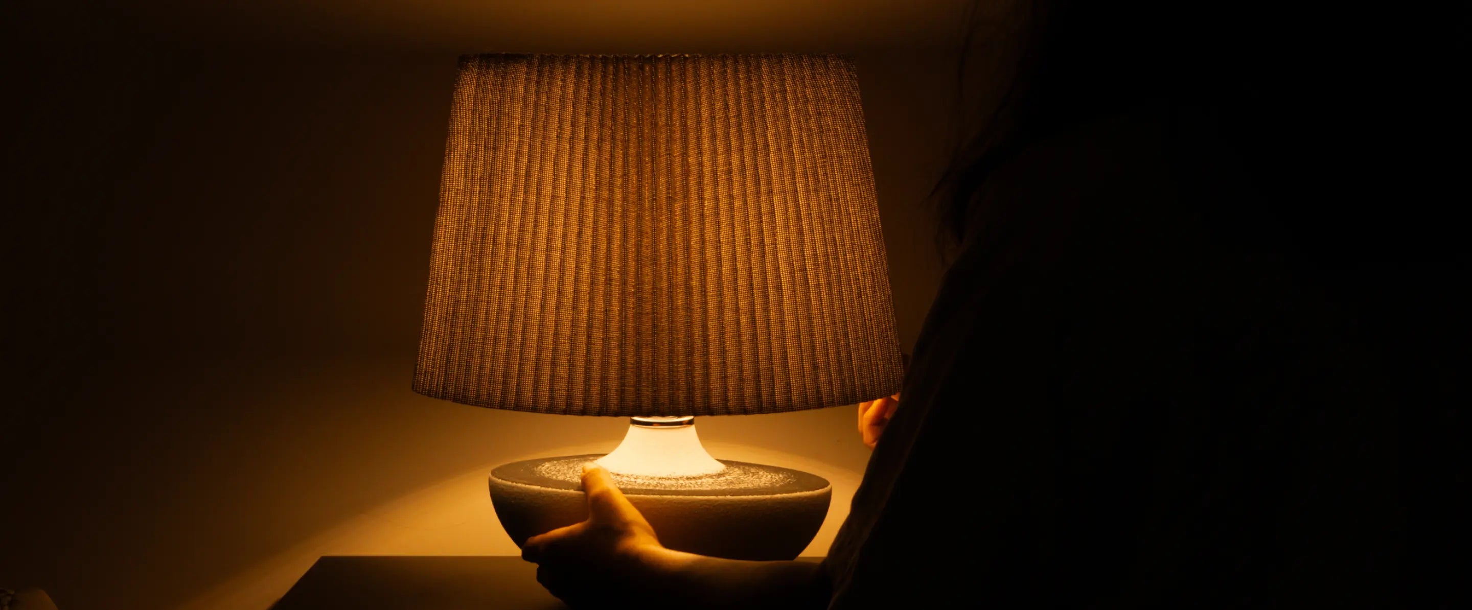 Hand holding ceramic table lamp glowing warmly in dark room