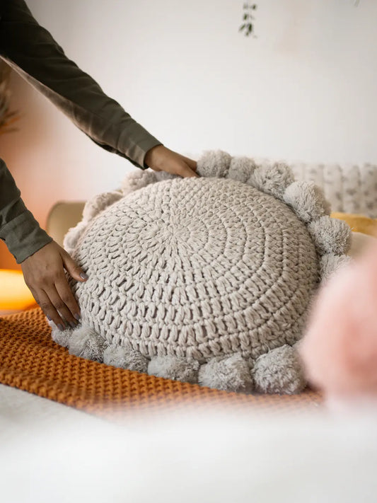 Hands placing a round knitted cushion with tassels on bed – stylish decorative cushion