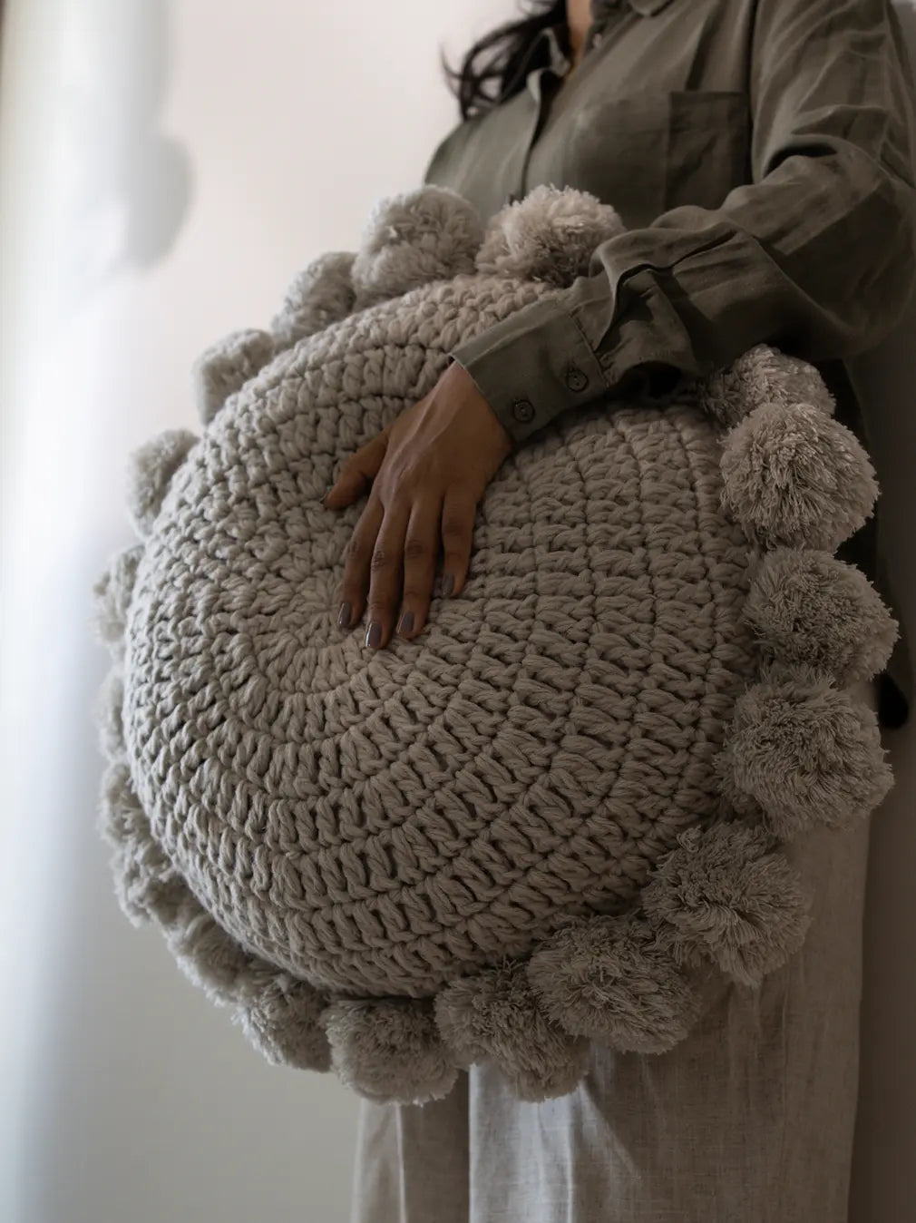 Person holding a fluffy round cushion with tassels – high quality decorative cushion for sofa.