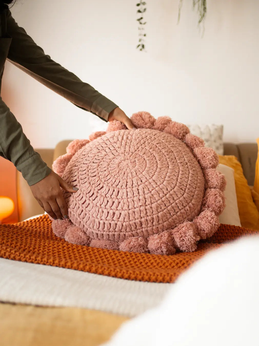Woman placing Nimbus Round Cushion Pink on bed for modern homes.