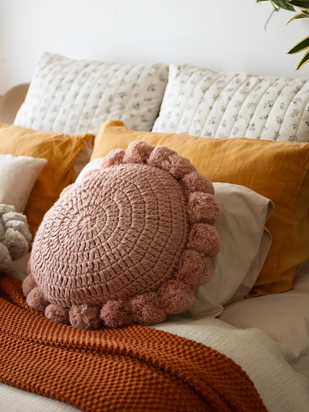 Decorative pillow with pom-pom details on a bed with colorful pillows and a blanket.
