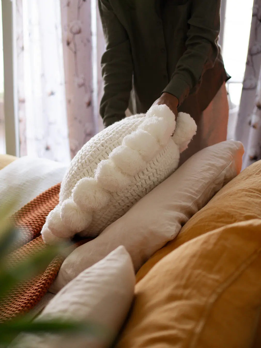 Person arranging decorative pillows on a couch with a focus on texture and color.