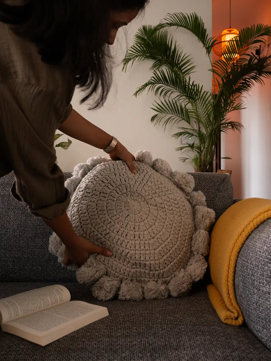Woman placing a Gharko grey round knitted cushion on a sofa for cozy home decor.