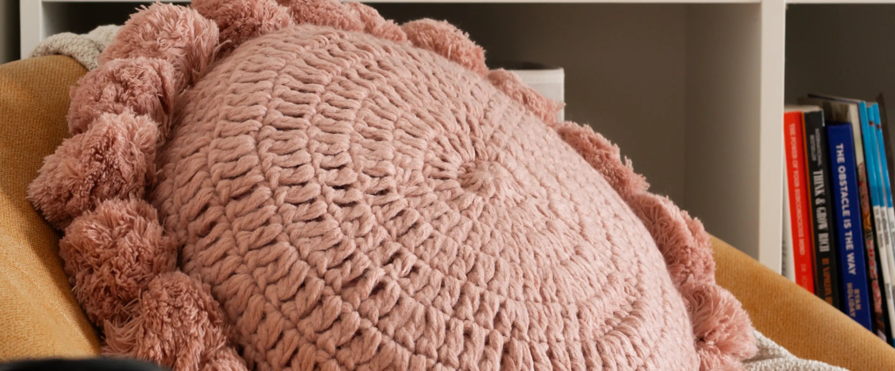 Pink sofa pillow on a couch with books in the background