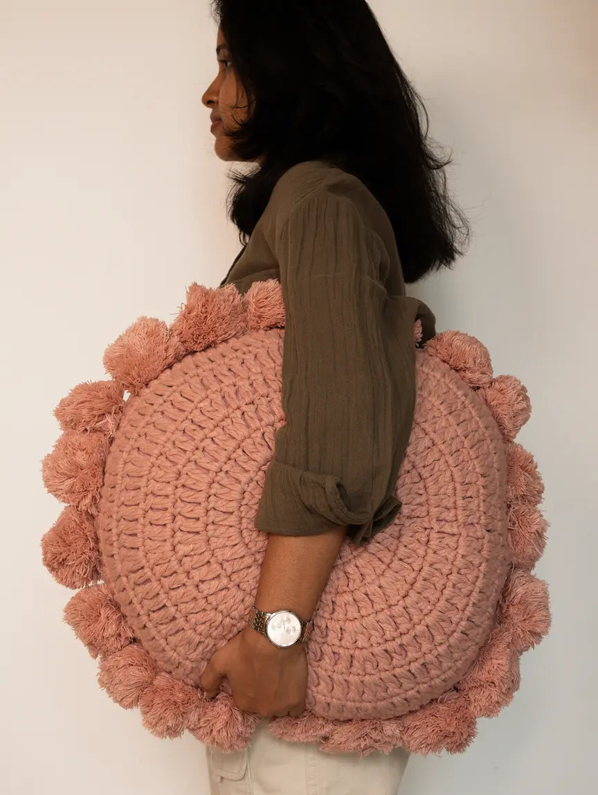 Person holding a large pink cushion with pom-poms against a plain background