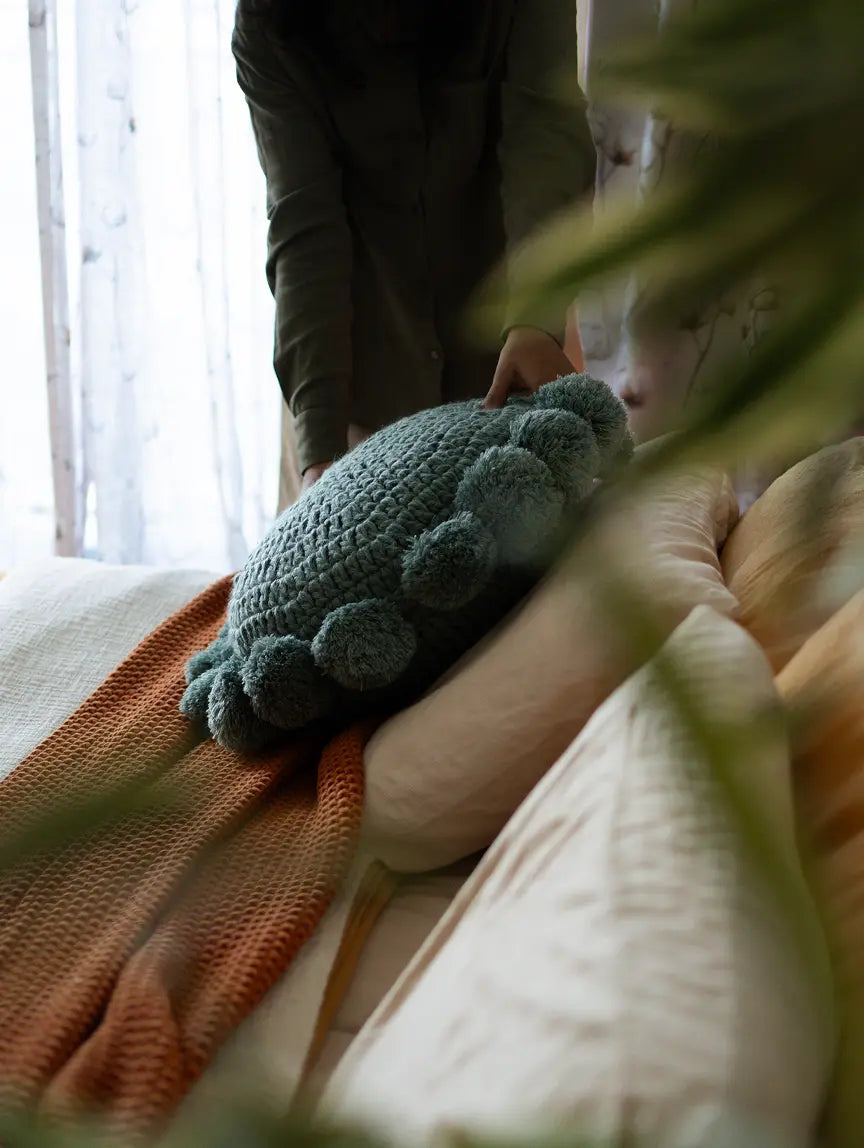 Person holding turquoise blue round knitted cushion with tassel