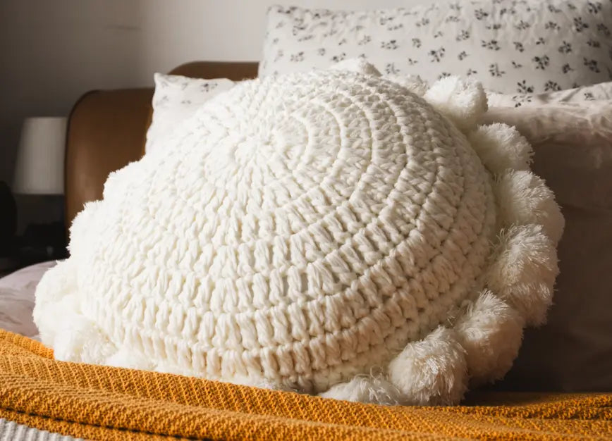 White textured pillow with pom-poms on a bed