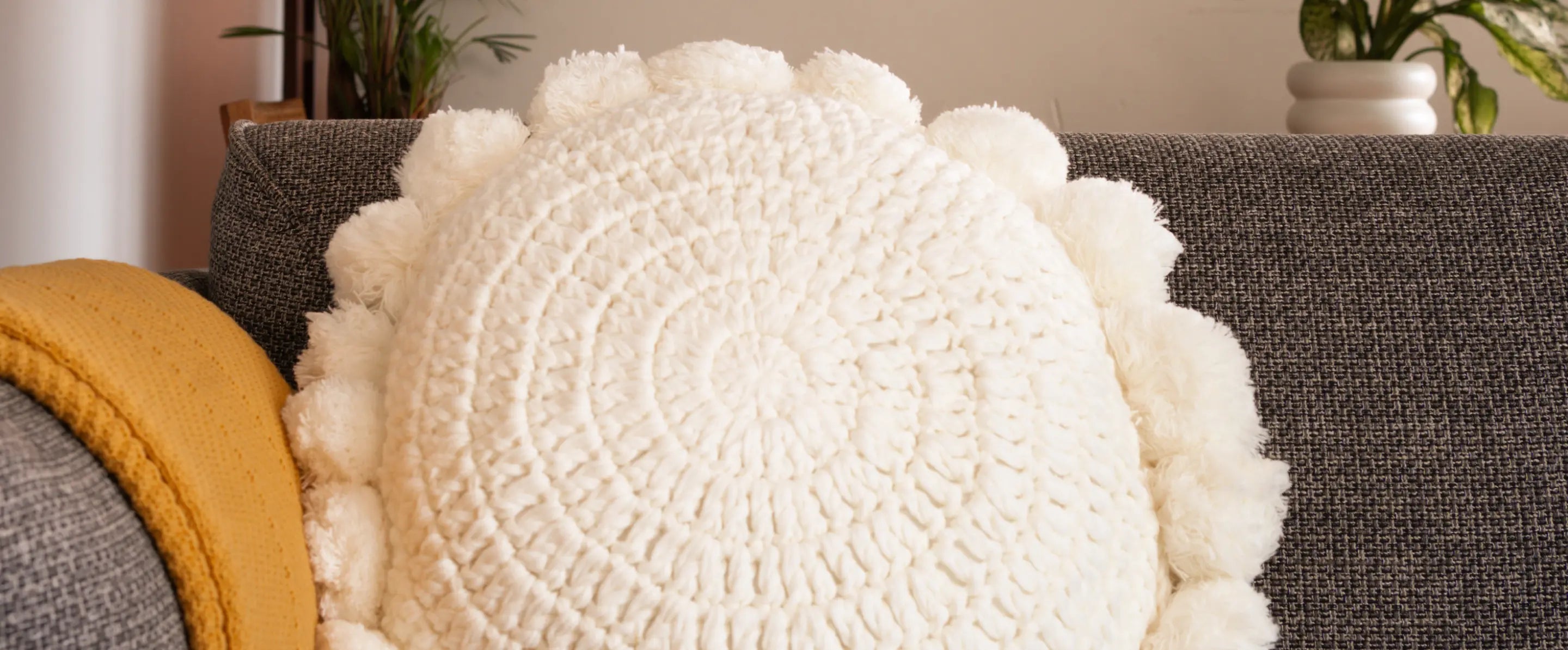 Round textured white pillow on a gray sofa with a yellow blanket