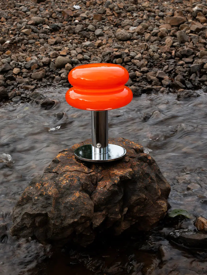 Orbit Red cordless table lamp with chrome base styled beside a rocky stream