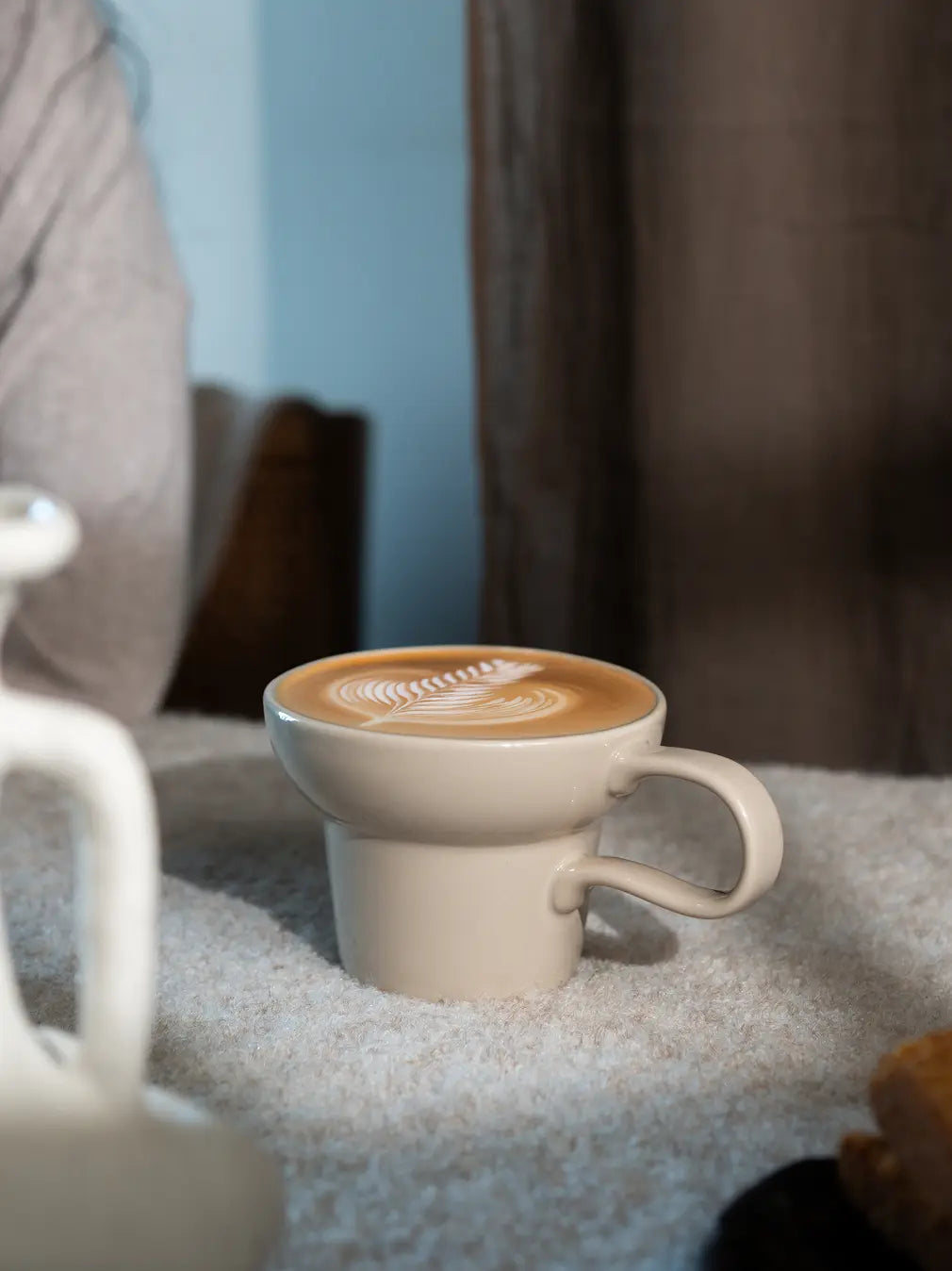Beige Pico ceramic coffee mug filled with latte, showcasing modern sculpted design