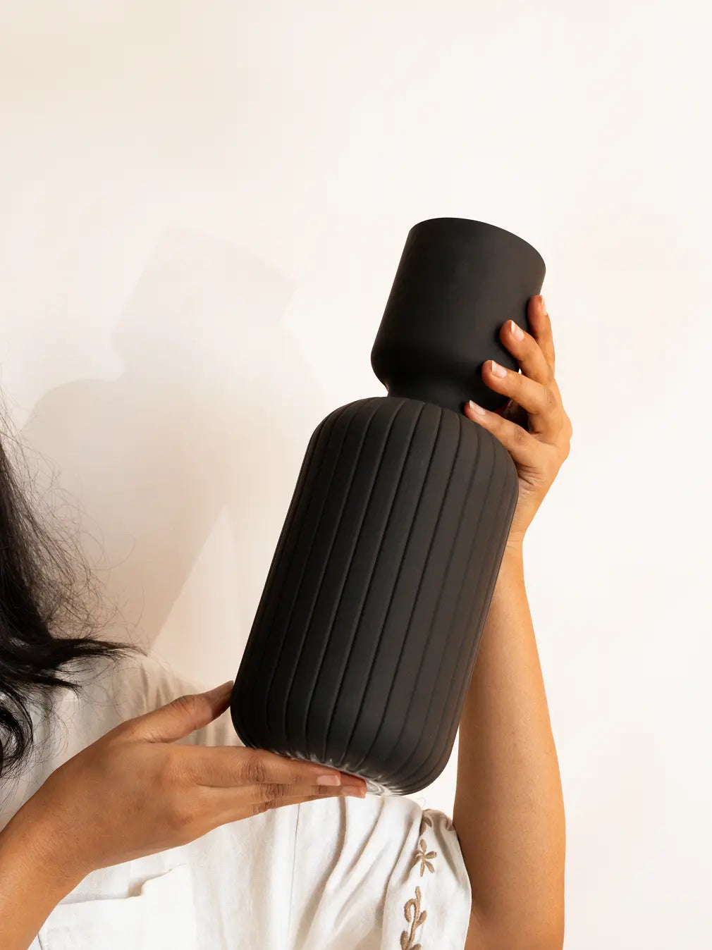 Person holding a textured black vase against a plain background