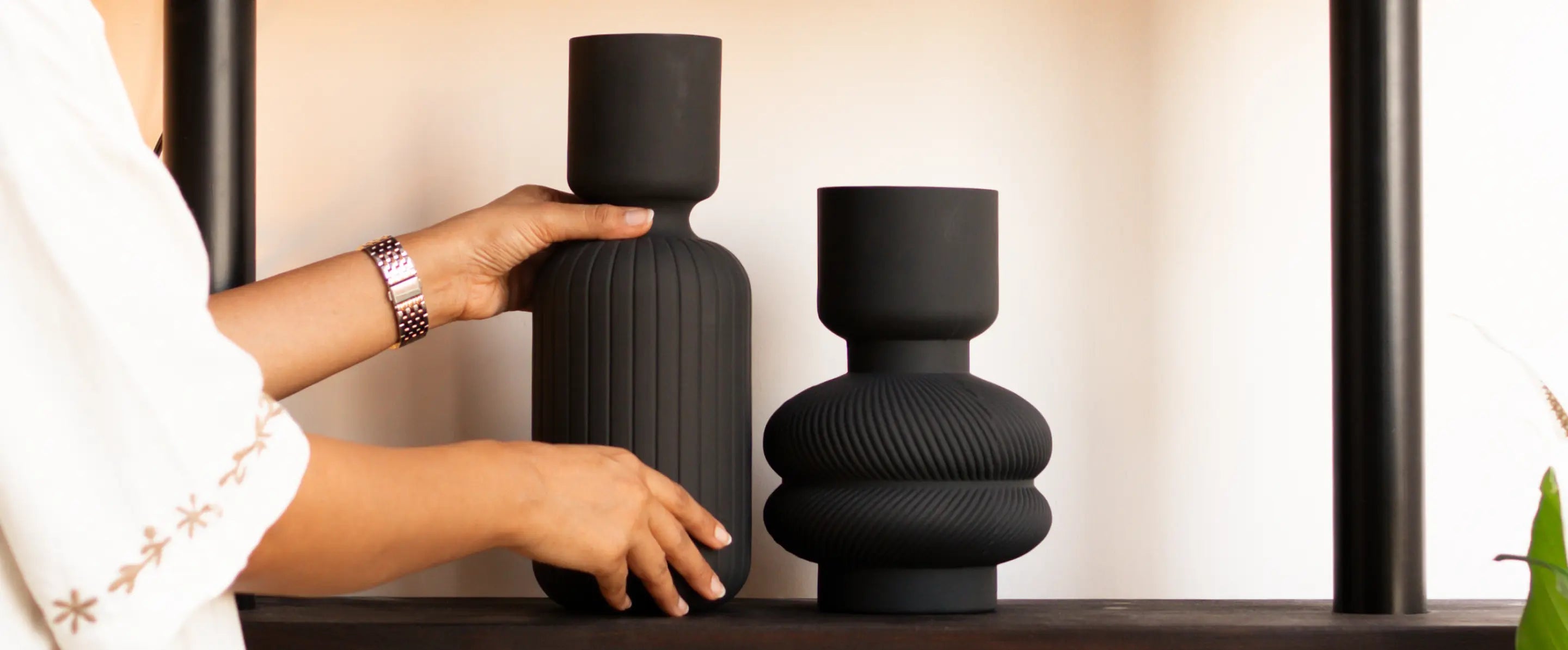 Person holding a textured black vase next to another similar black vase on a surface.