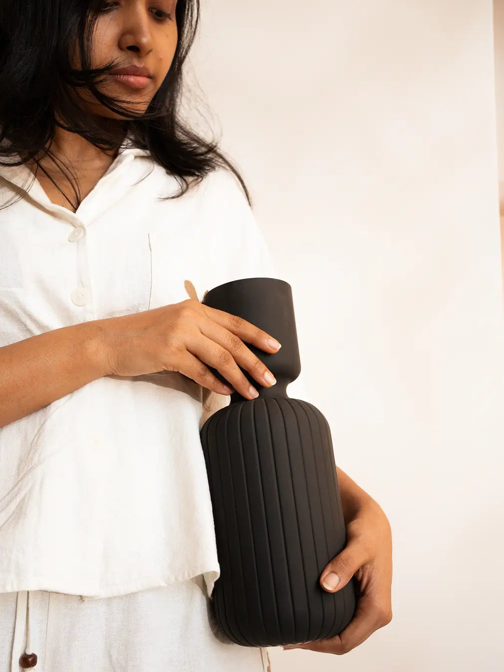 Person holding a black flower vase against a plain background