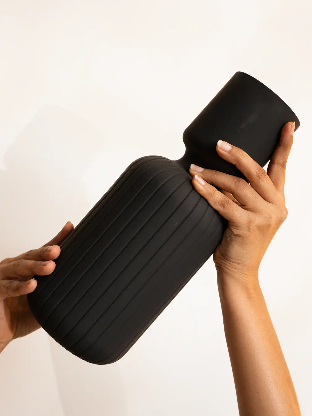 Hands holding the Ridge Glass Vase, showing its ribbed body and modern matte black finish.