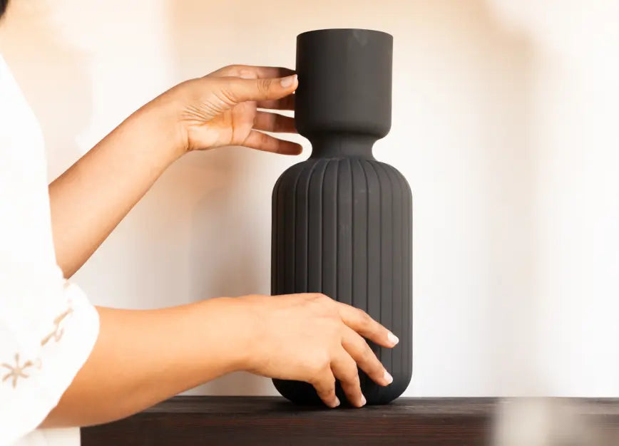 Person holding a textured black vase on a wooden surface
