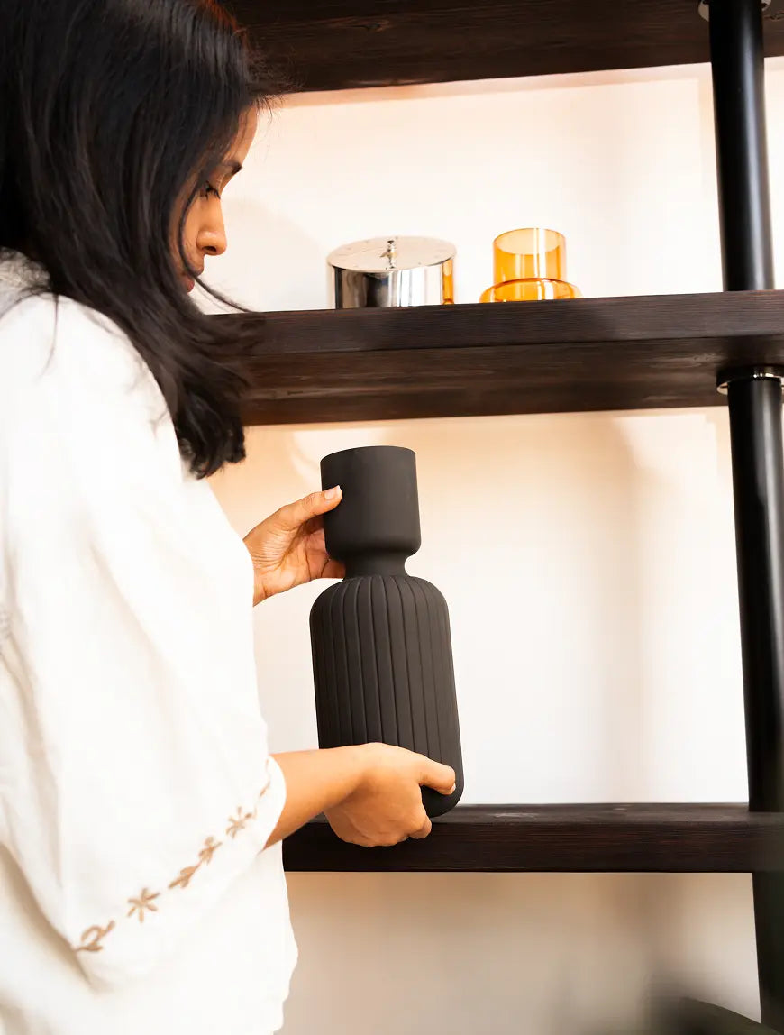 Hands placing the Ridge Glass Vase on a shelf, showing its matte black modern ribbed design