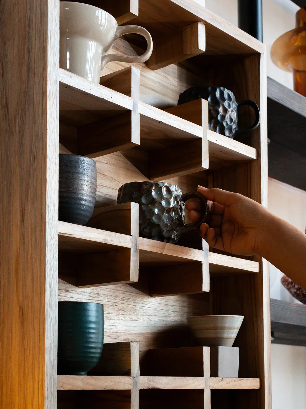 Hand placing mug on teak wood coffee cup shelf wall rack with grid compartments
