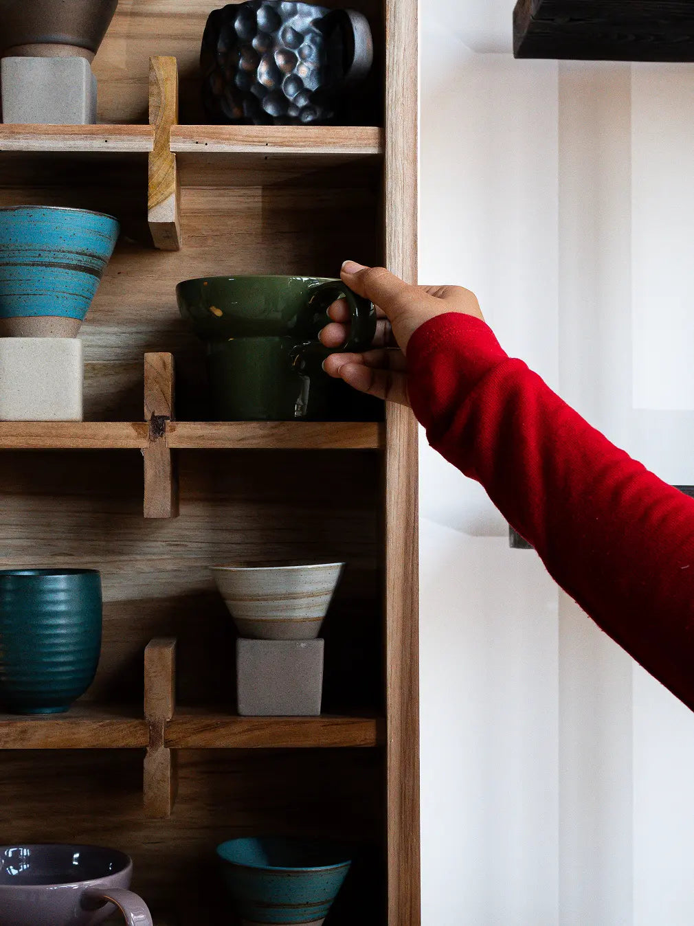 Hand placing coffee mug on teak wood wall-mounted cup shelf organizer