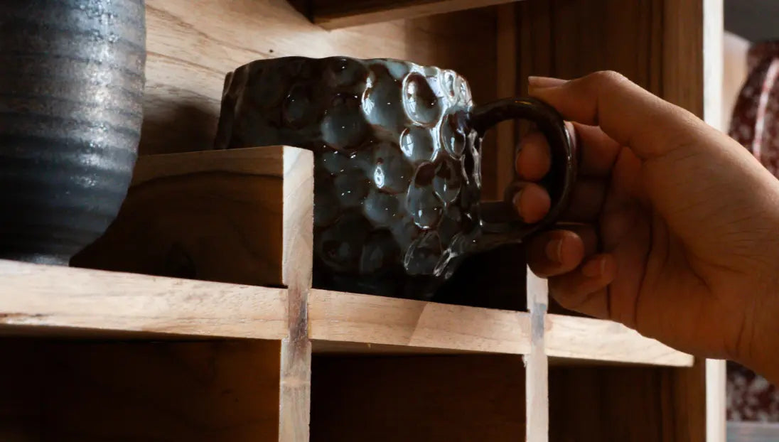 Hand placing textured mug on teak wood coffee mug display shelf