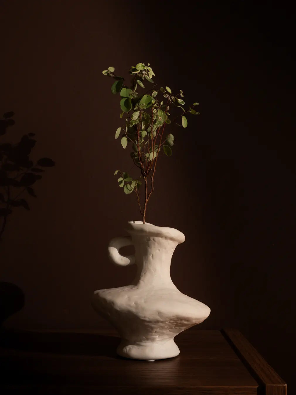 Suki Mini Ceramic Vase styled with greenery on a wooden table, featuring an organic white porcelain finish.