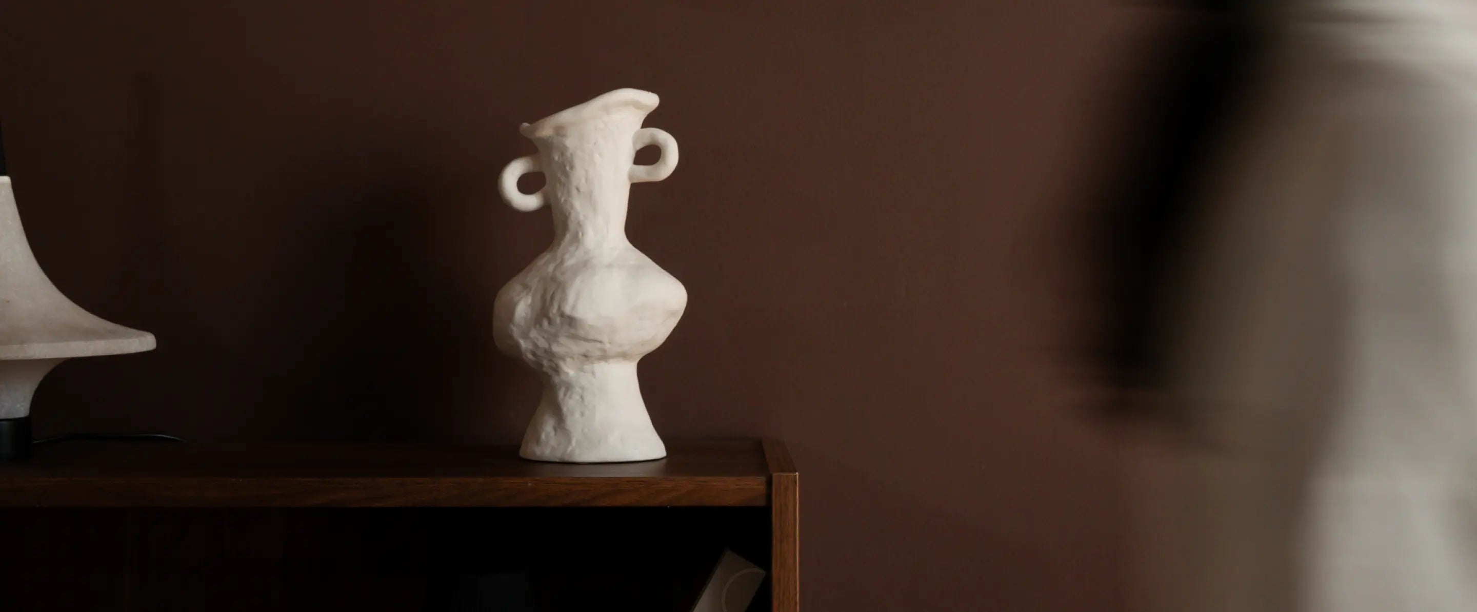 Suki Ceramic Vase styled on a wooden shelf against a brown wall