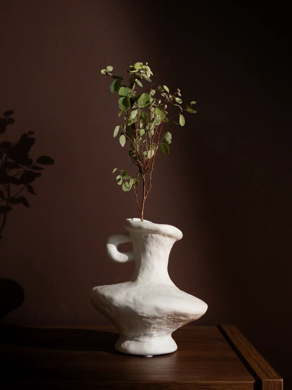 Suki Mini Ceramic Vase styled with greenery on a wooden table, featuring an organic white porcelain finish.