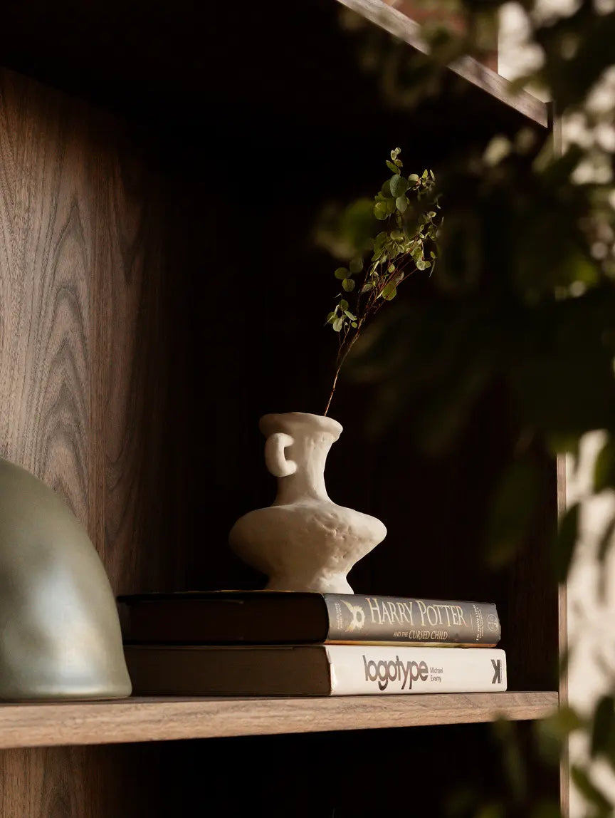 Suki Mini Ceramic Vase styled on a wooden shelf with greenery, highlighting its organic white sculptural form.