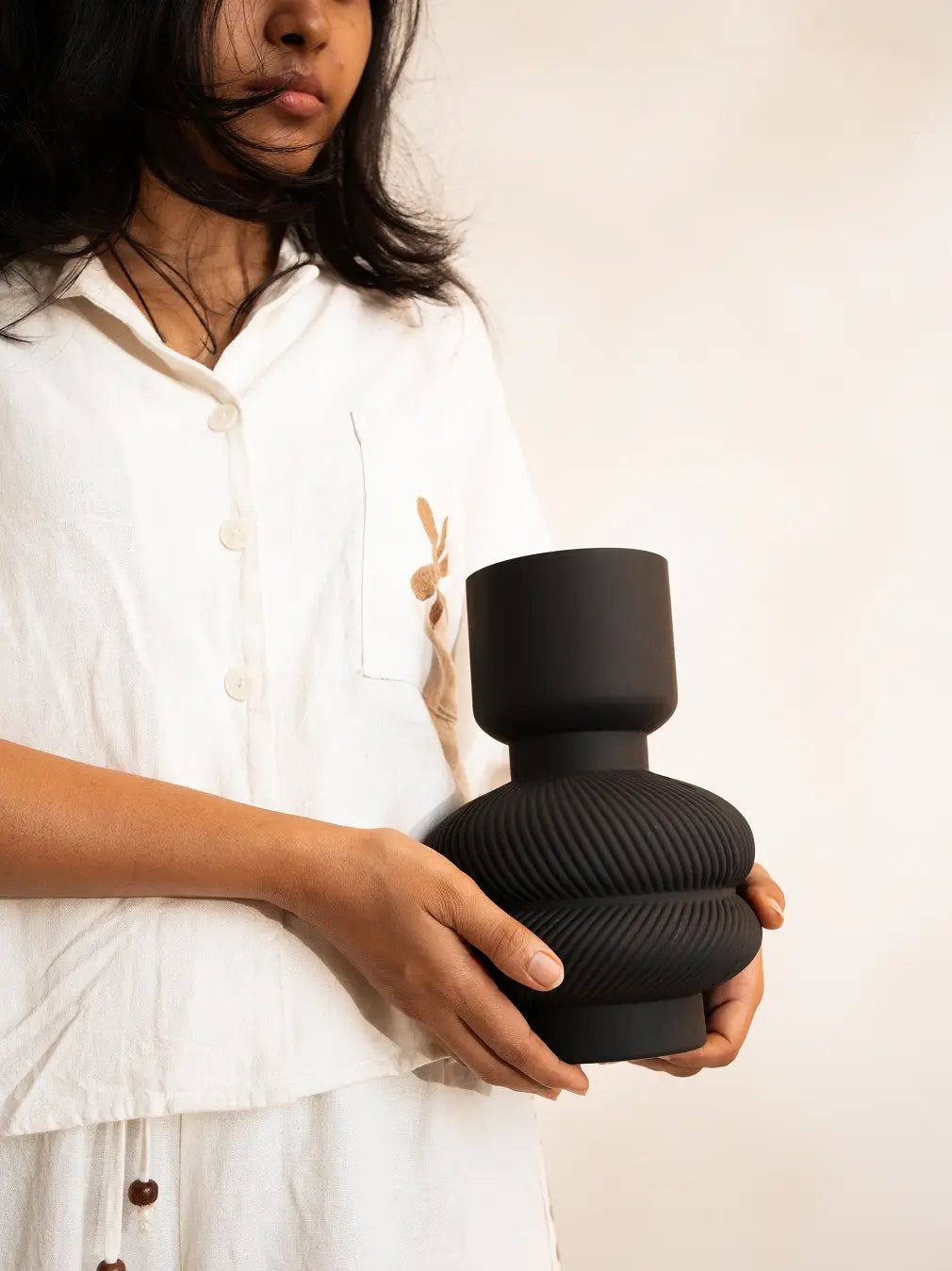 Person holding a textured black vase against a plain background