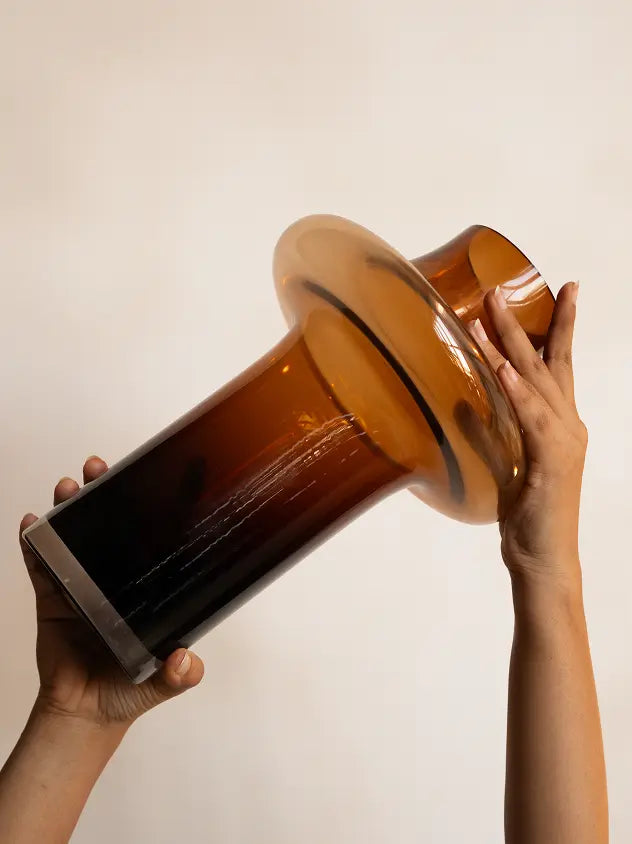 Person holding a large brown glass vase against a plain background