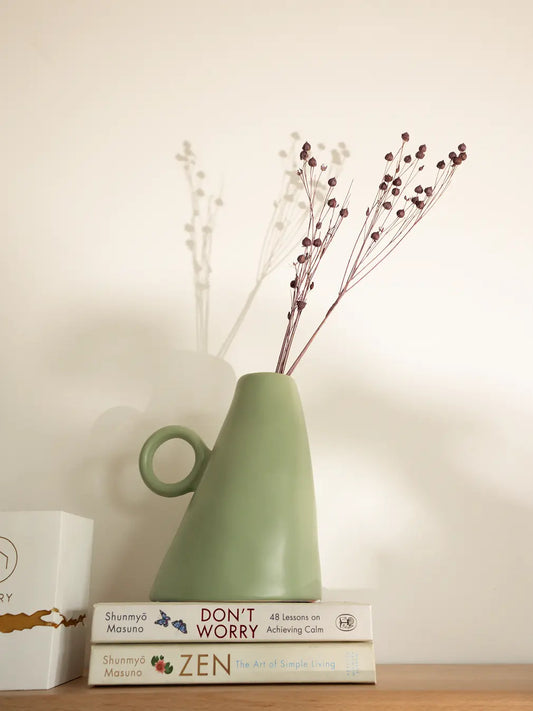 Green ceramic vase on books, decorative modern vase for flowers.
