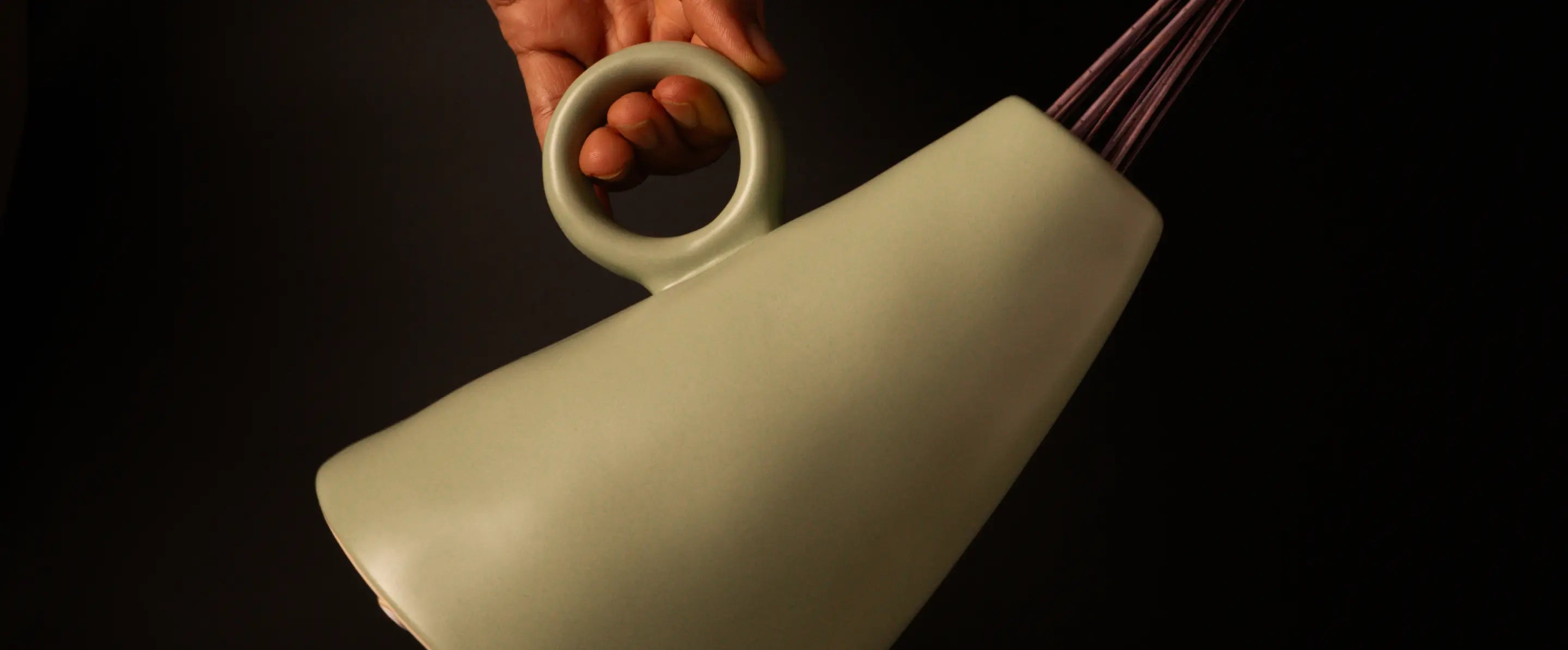 Ceramic vase with a handle held by a hand against a dark background