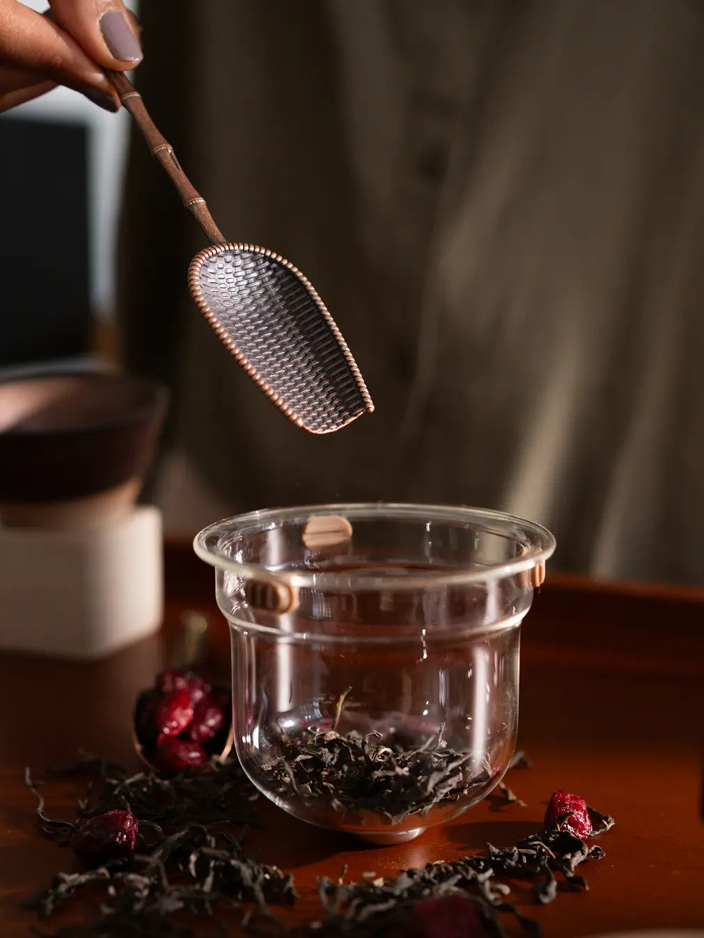 Hand holding a Vintage Spoon, scooping loose-leaf tea into a glass brewing pot.