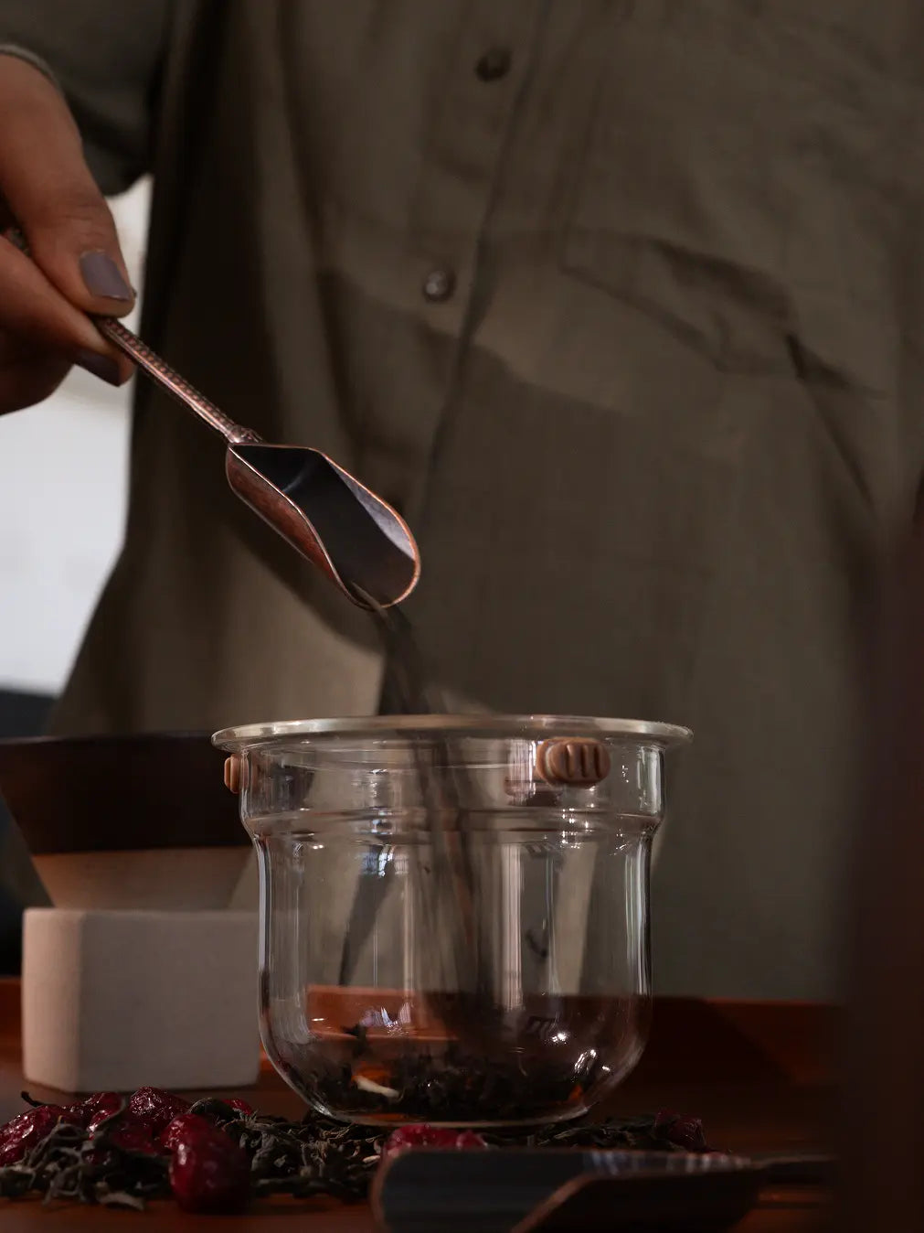 Hand using the Vintage Spoon to scoop loose-leaf tea into a glass teapot.