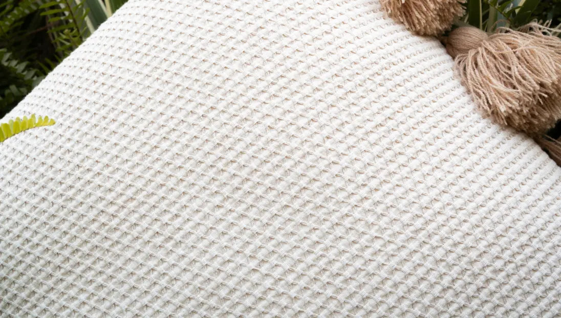 Close-up of a textured Waffle cushion cover with a tassel on a blurred natural background