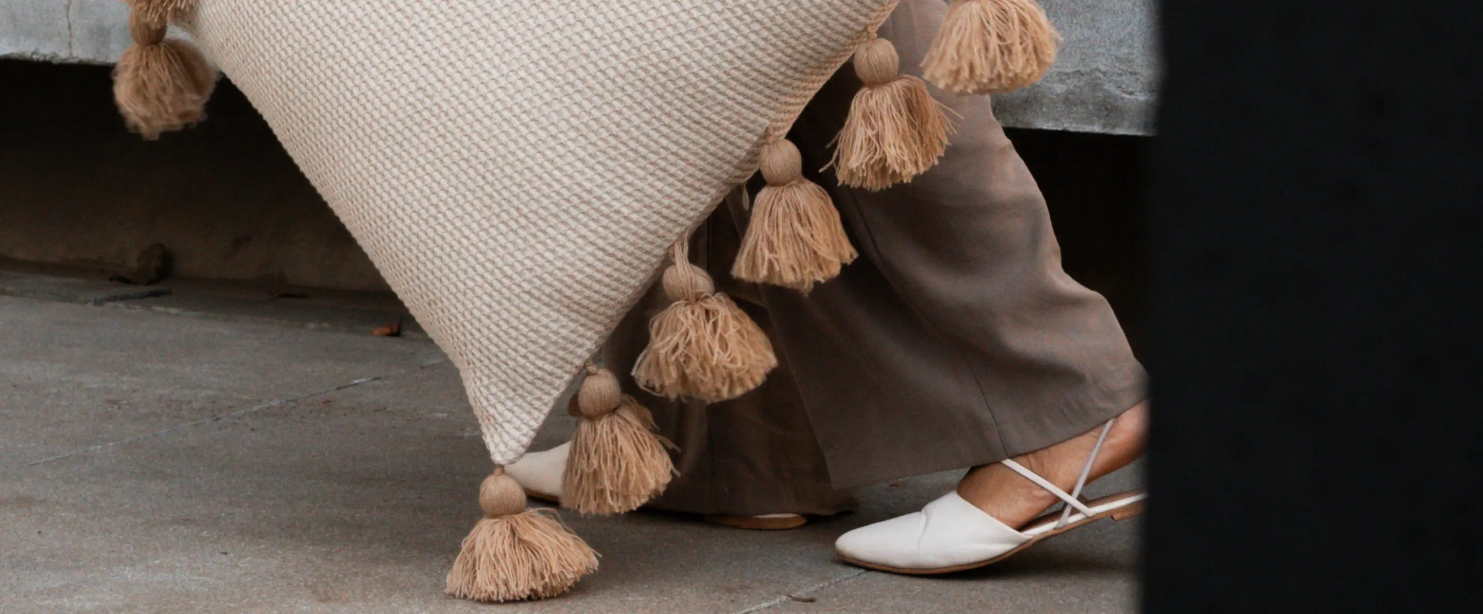 Close-up of a designer pillow with tassels and a person wearing earthy dress