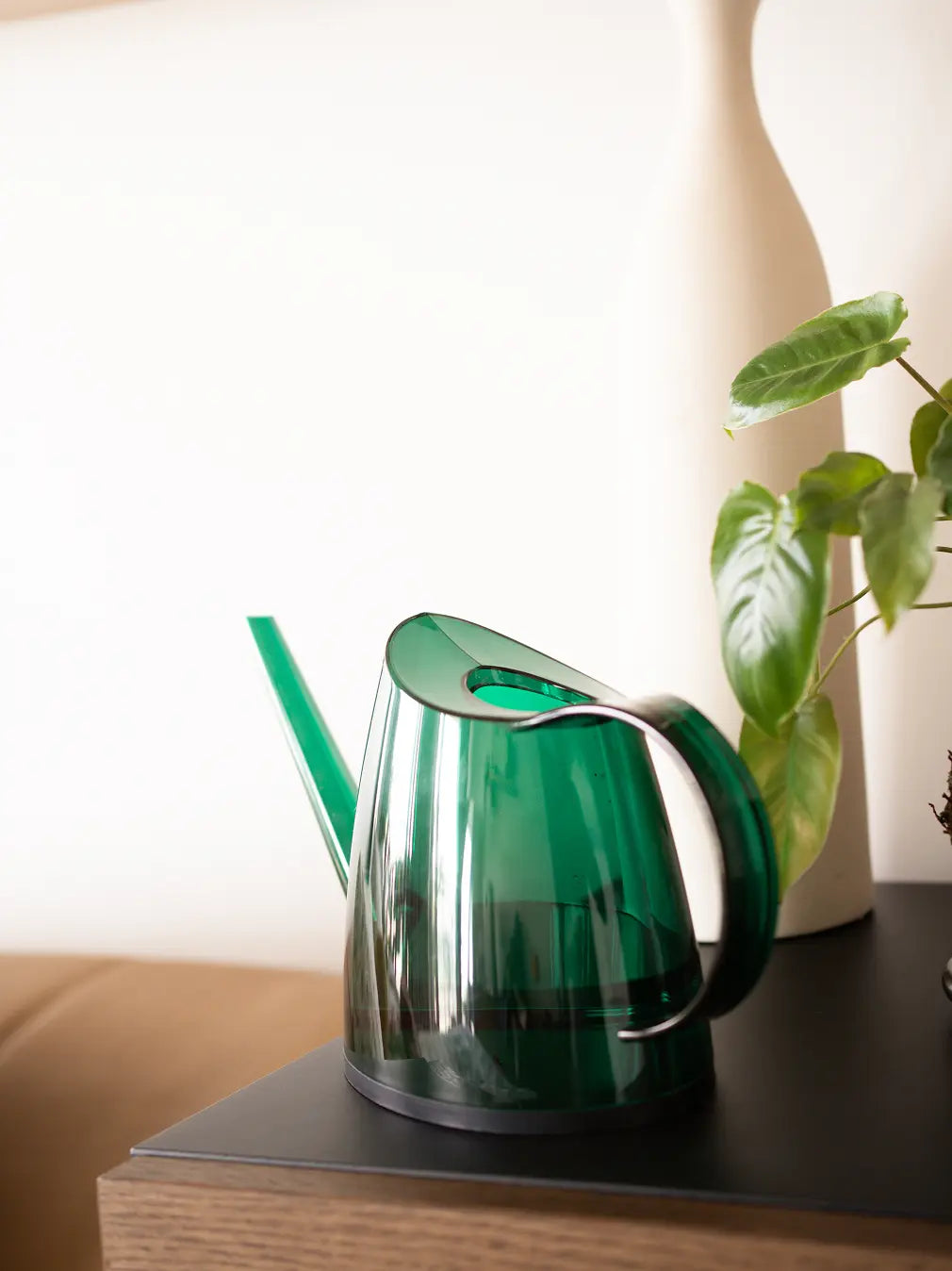 Green Willow Watering Can placed on a shelf beside indoor plants, showing its modern shape.
