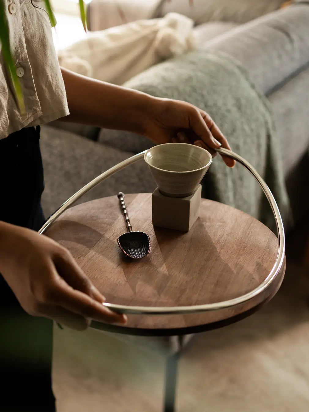 Person holding modern wooden tray with ceramic cup and spoon