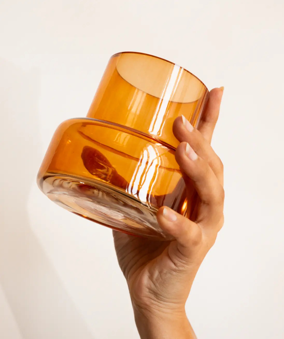 Hand holding an orange glass container against a light background